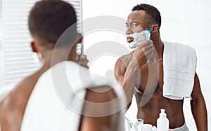 Shirtless Black Guy Shaving Face In Morning Standing In Bathroom