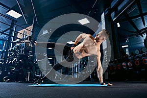 Shirtless bodybuilder doing side plank exercise.