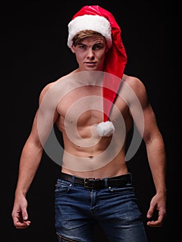 Shirtless bodybuilder in a santa cap on a black background. male Santa. Christmas party concept.