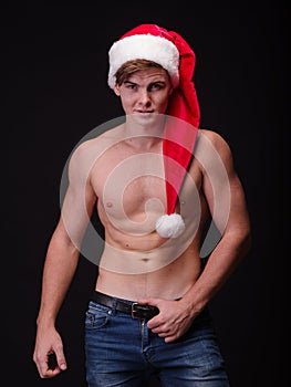 Shirtless bodybuilder in a santa cap on a black background. male Santa. Christmas party concept.