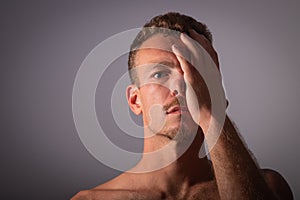 A shirtless boy covers half of his face and looks towards the camera. Thoughtful and spiritual man