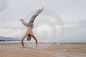 Shirtless caucasian man doing backflip on pebble beach.