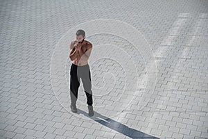 Shirtless caucasian man is getting cold and holding his hands near his face outdoors.