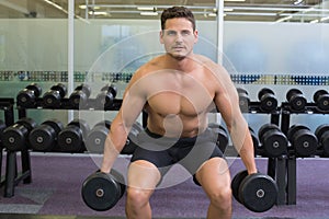 Shirtless determined bodybuilder lifting heavy black dumbbells