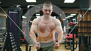 Shirtless handsome athletic man doing pectorals on the crossover trainer in the gym. Shot in 4k