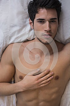 Shirtless male model lying alone on his bed