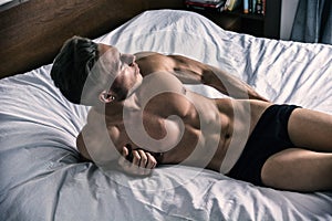 Shirtless male model lying alone on his bed
