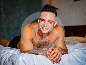 Shirtless male model lying alone on his bed smiling