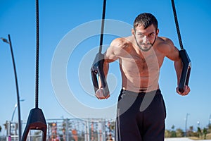 Shirtless man doing loop exercises outdoors.