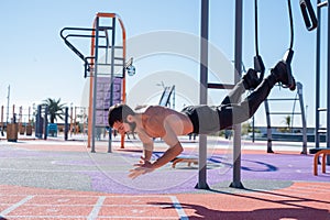 Shirtless man doing loop exercises outdoors.