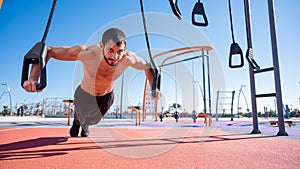 Shirtless man doing loop exercises outdoors.