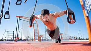 Shirtless man doing loop exercises outdoors.