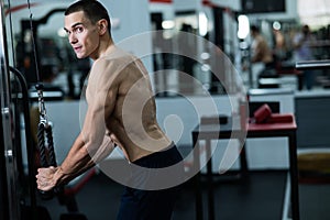 Shirtless man doing triceps pulldown at the gym.