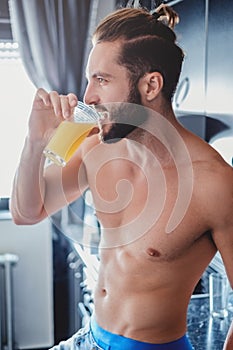 Shirtless man drinking orange juice in the kitchen