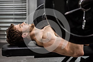 Shirtless man lifting heavy barbell on bench