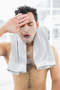 Shirtless man yawning with eyes closed in bedroom