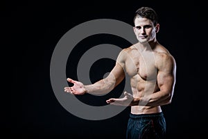 Shirtless muscular athletic man point with two hands to blank copyspace. bodybuilder showing his body on black