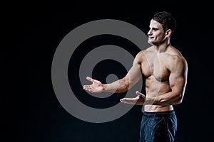 Shirtless muscular athletic man point with two hands to blank copyspace. bodybuilder showing his body on black