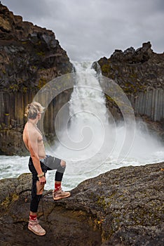 Shirtless and muscular boy looks at the Aldeyjarfoss waterfall in Iceland