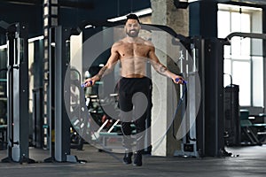 Shirtless muscular guy jumping with skipping rope in gym