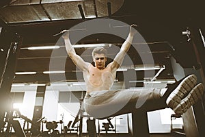 Shirtless muscular handsome young man doing exercises on horizontal bar in a gym club.