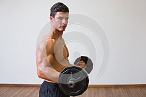 Shirtless muscular man lifting barbell in gym