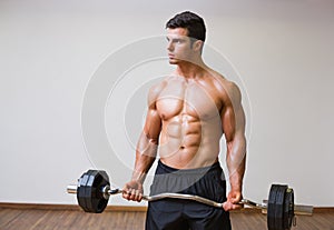 Shirtless muscular man lifting barbell in gym