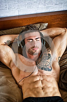 Shirtless muscular sexy male model on bed, relaxing with eyes closed