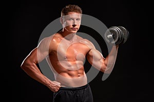Shirtless muscular sportsman pumping up biceps with black dumbbell