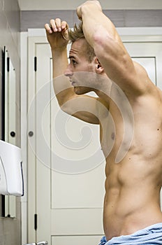 Shirtless, muscular young man looking at his hair