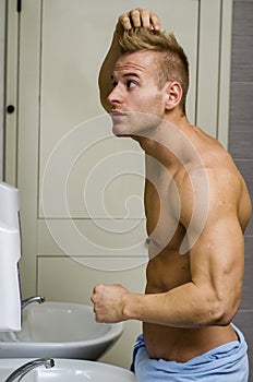 Shirtless, muscular young man looking at his hair in bathroom mi