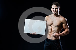 Shirtless muscular young man standing holding a blank horizontal white banner pointing finger at the copyspace for your