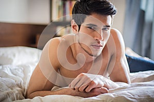 Shirtless male model lying alone on his bed