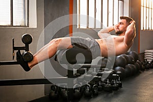 Shirtless strong man performing GHD sit up exercise for abs in gym