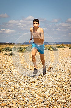 Shirtless teenage boy running on a beach