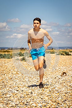 Shirtless teenage boy running on a beach