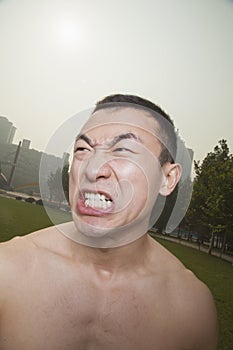 Shirtless young athletic man growling outdoors in a park in Beijing