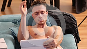 Shirtless young athletic man reading on ebook reader