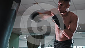 Shirtless young man boxer training with a punching bag