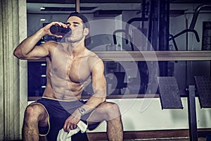 Shirtless young man drinking protein shake in gym