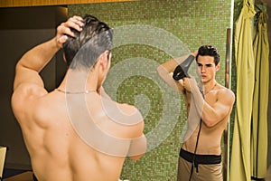 Shirtless young man drying hair with hairdryer