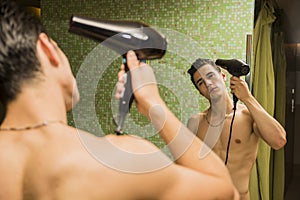 Shirtless young man drying hair with hairdryer