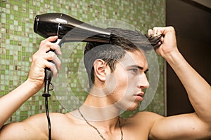 Shirtless young man drying hair with hairdryer