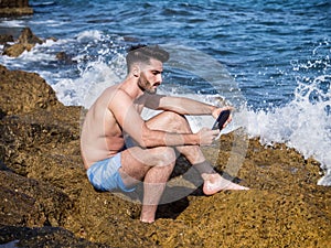 Young man on beach reading with ebook reader