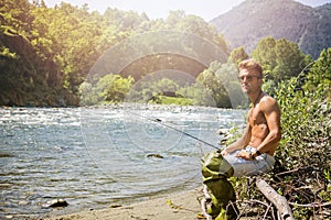 Shirtless young man fishing with rod at river