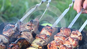 Shish kebab on the grill close-up. Fried meat on skewers is visible. The woman adjusts the skewers and sprinkles the kebab with