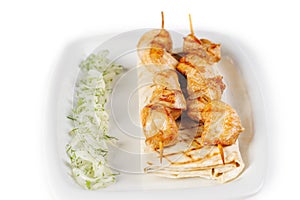 Shish kebab on a skewer with lavash, onions and greens on a white plate on white isolated background