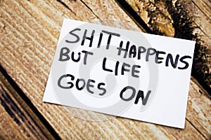 Shit happens but life goes on handwritten message on white paper with retro wooden bark background. Motivational handwritten messa