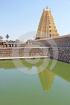 Shiva Virupaksha Temple and green pond, green water. Hampi, Karnataka, India. White yellow restored temple against the blue sky.