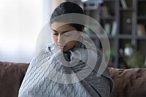 Shivering indian female teenager trying to warm up under plaid